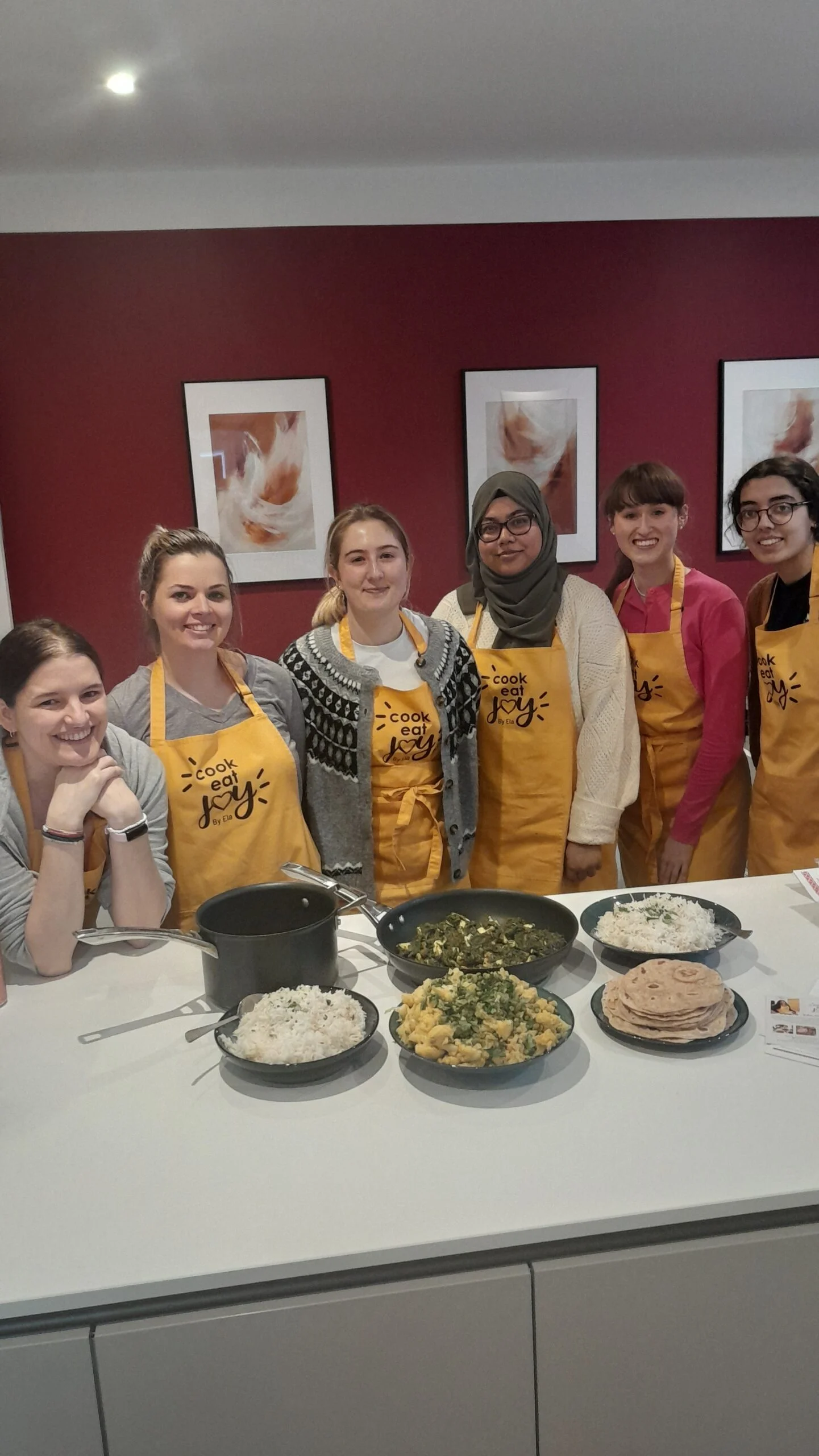 Six women in Cook Eat Joy yellow aprons smiling in class