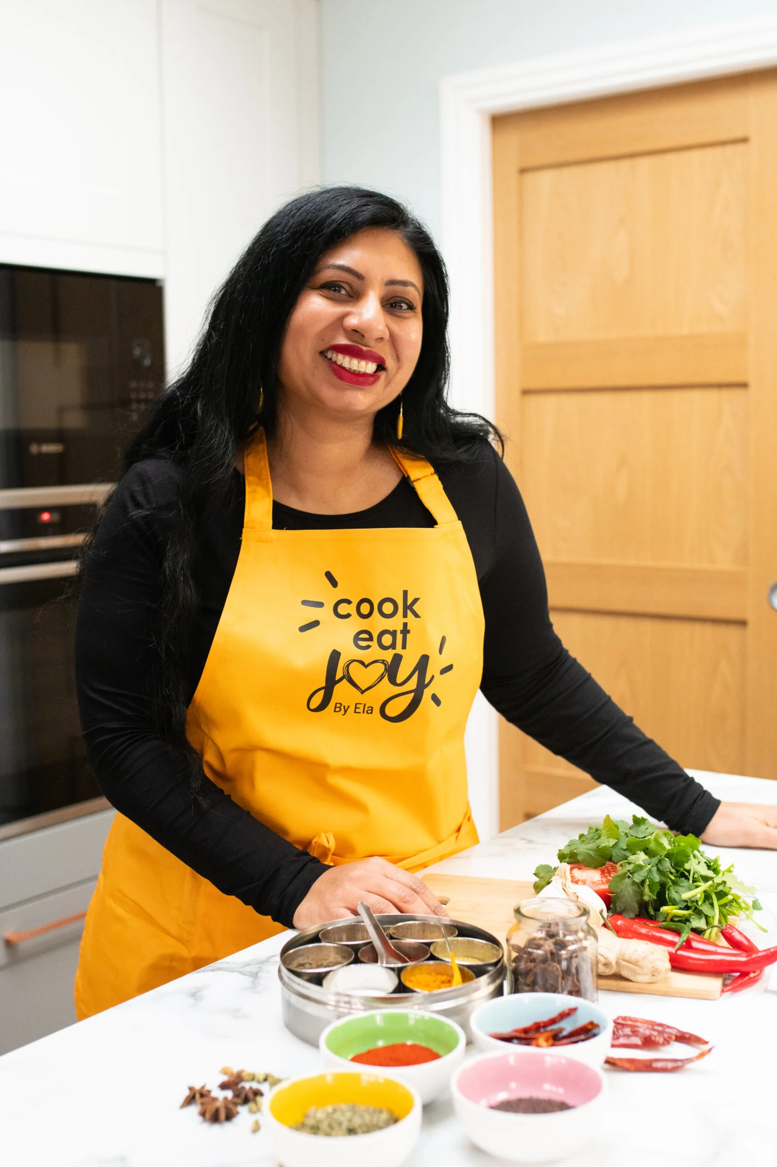 Ela in her yellow Cook Eat Joy apron with spices